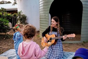 Kat Kellalea playing guitar for a couple of children